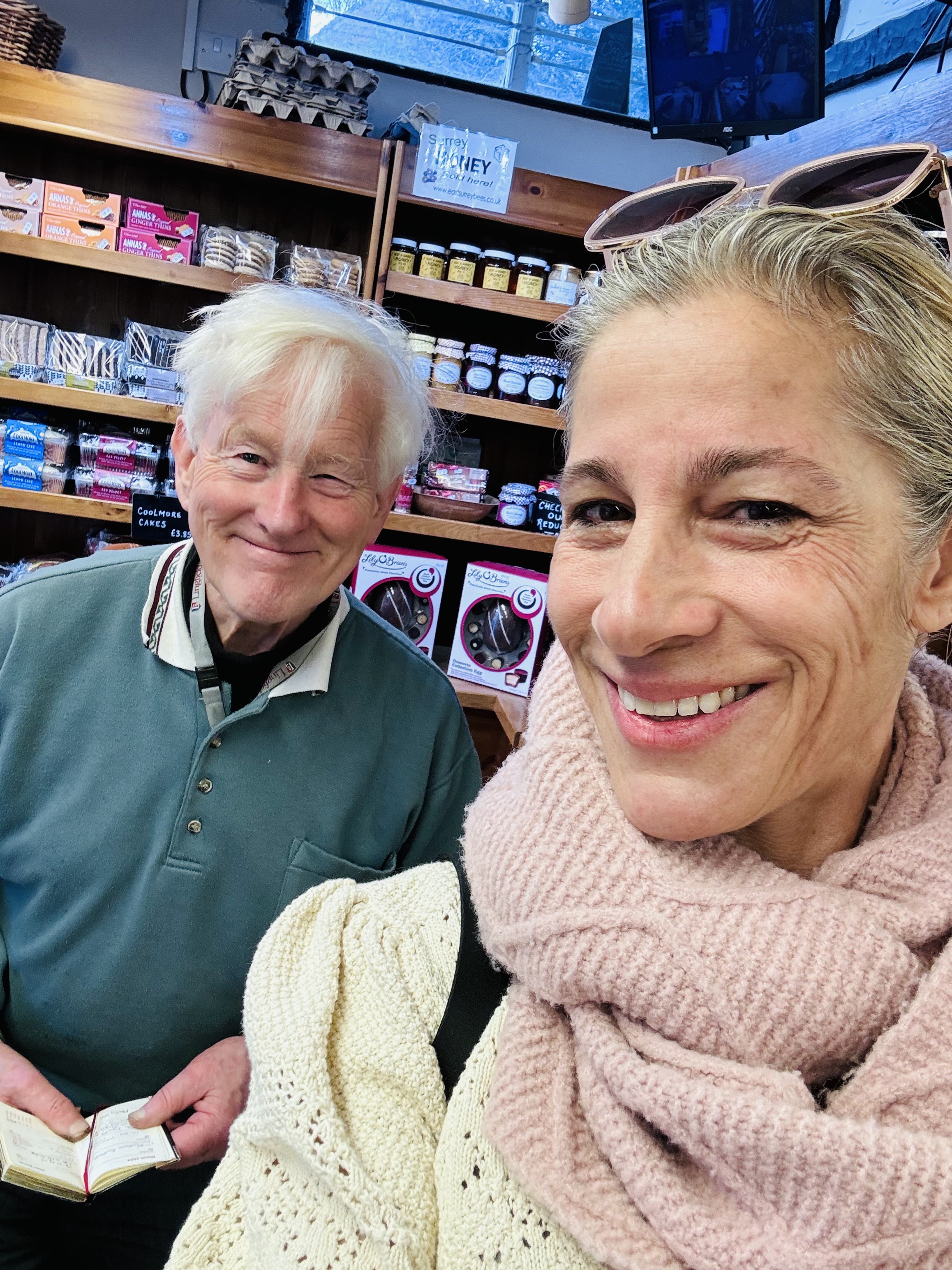 Smiling older man and woman in a pink scarf taking a selfie inside a shop